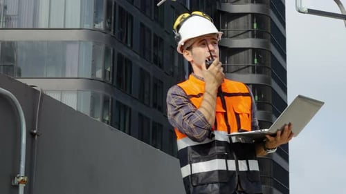 Vorarbeiter arbeitet auf der Baustelle und überwacht die Antenne, überprüft den Laptop und telefoniert im Funkruf