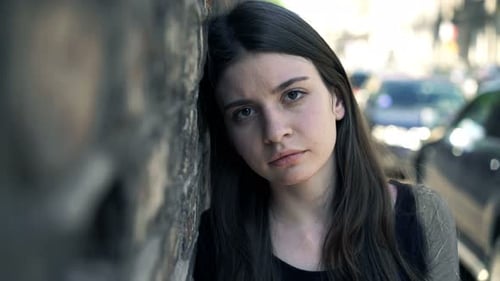 Sad young woman leaning against brick wall in urban city despair portrait