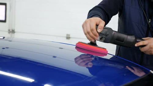 A Man Polishes a Blue Car with a Car Polishing Machine at a Car Dealership