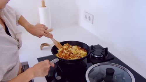 Woman Cooking Food in Pan with Wooden Spoon