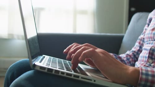 Man Works on a Laptop While Sitting on the Couch at Home