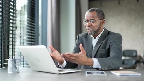 Un homme d'affaires afro-américain bouleversé et inquiet lit de mauvaises nouvelles sur un ordinateur portable assis à son bureau sur son lieu de travail