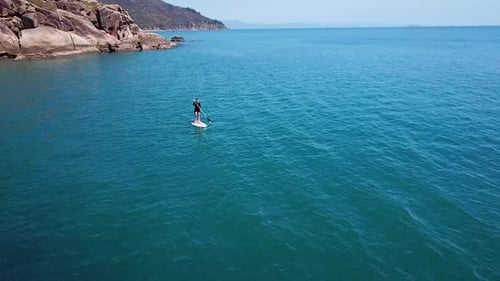 Drohnenaufnahmen aus der Luft kreisen um eine einsame Frau, die auf einer abgelegenen Insel auf eine Luxusyacht zupaddelt