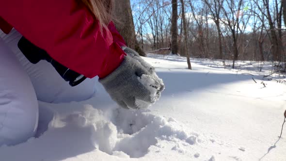 Close up of a girl making a snowball with a DSLR camera strapped around ...