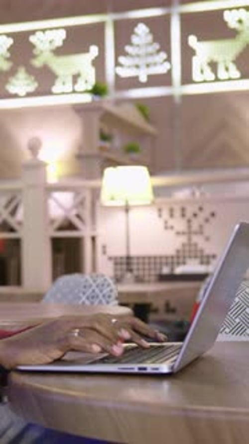 Person Using Laptop on Wooden Table in Modern Cafe with Stylish Decor and Ambient Lighting