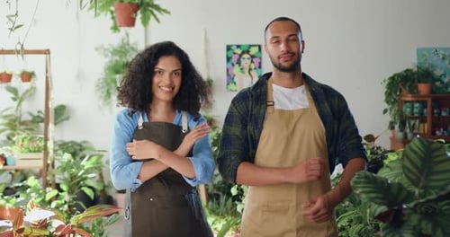 Cheerful woman and man florists looking to camera in flower store standing together smiling.