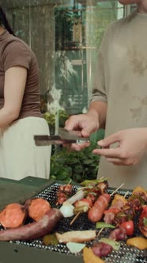 Vertical of Young People Cooking Skewers on Grill Outdoors