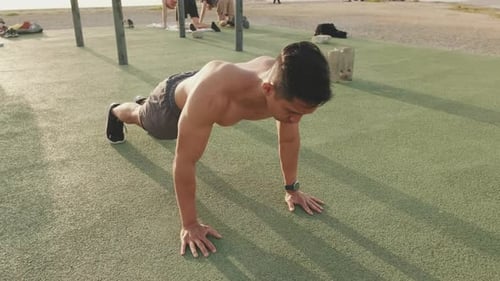 Young man doing push-ups on a sports ground by the sea