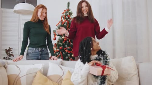 Three Young Women Exchange Christmas Gifts at Home