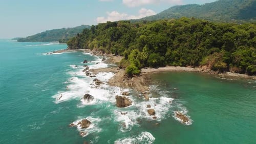 Rocky jungle coast at tropical beach with scenic view of ocean waves in slow motion