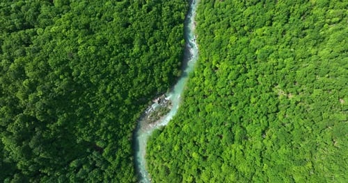 A bird's eye view of a wild mountain river of pure greenish color. The river flows between two mount