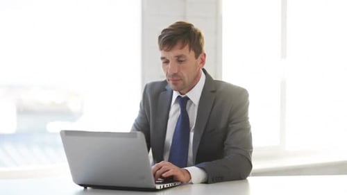Handsome businessman works with laptop computer in modern office setting
