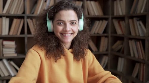Smiling woman studies with laptop and headphones at desk