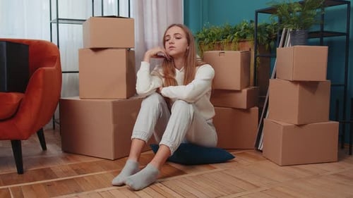 Mujer molesta sentada en el suelo cerca de cajas de cartón con cosas por larga reubicación, quiebra, deuda bancaria