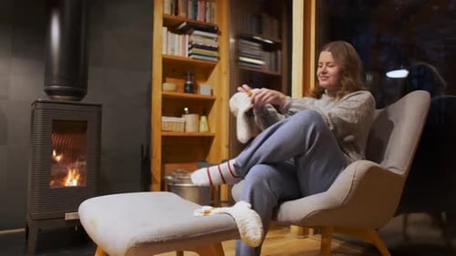 Woman Puts on Socks by Fireplace on Winter Night