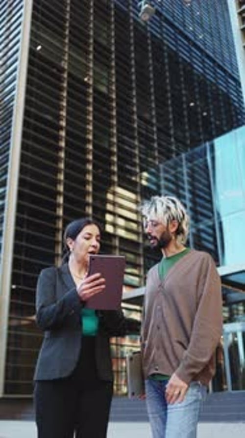 Two business people having a discussion while using a digital tablet outside the office