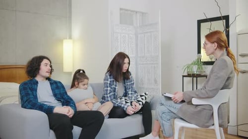 En un apartamento acogedor y luminoso, una joven psicóloga habla con una familia que parece triste y triste
