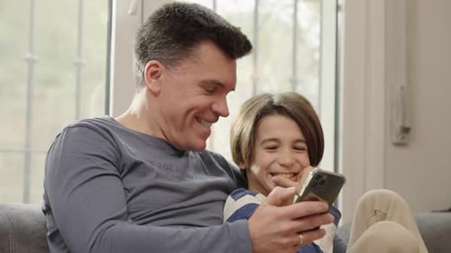 Father and Child Laughing at Smartphone Indoors
