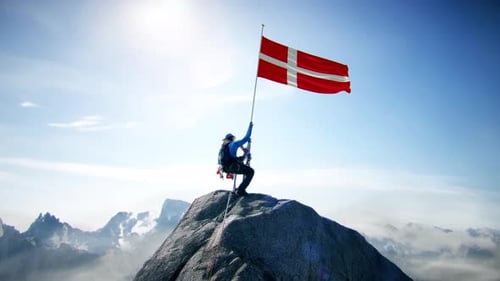 Montañero con la bandera de Dinamarca en la cima del vértice de la montaña