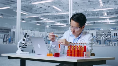 Asian Man Scientist Carrying Out Experiment Test Tube, Typing On A Laptop In Lab