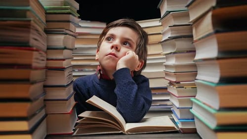 Verträumter kleiner Junge, der am Klassenzimmer oder am Schreibtisch in der Bibliothek sitzt, kluges Kind, das ans Lernen oder vielleicht denkt