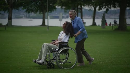 Senior Pushing Adult in Wheelchair Through Park