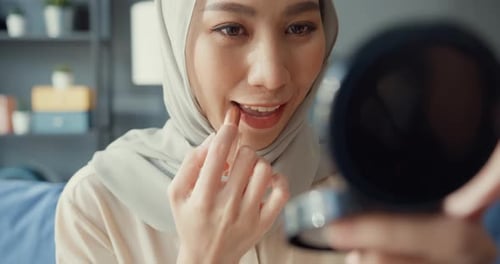 woman in hijab with casual sitting on couch enjoy applying make up lipstick on her lips.