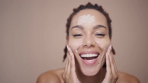 Woman Applies Facial Cream, Smiling Happily