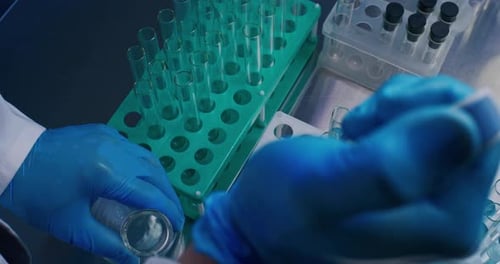 Professioneller Wissenschaftler gießt mit Pipette Flüssigkeit aus Glaskolben in Reagenzgläser