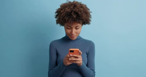 Smiling Woman Texting on Smartphone Against Blue Background