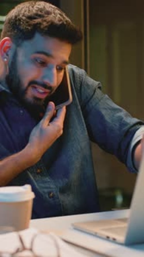 Téléphone parlant émotionnel multitâche pour homme d'affaires arabe occupé travaillant avec un ordinateur portable au bureau en soirée