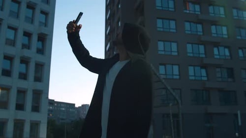 Hooded Man Tests Phone Reception in Cityscape