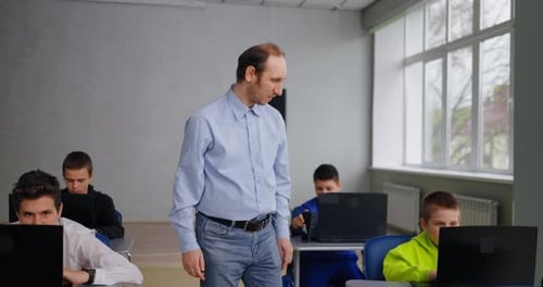 Teacher Supervising Students Using Laptops in Classroom