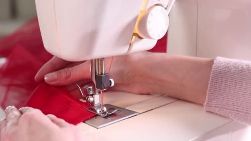 Woman sewing red fabric with professional machine in workshop, closeup