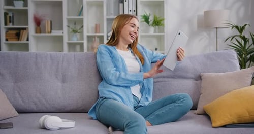 Hermosa joven caucásica sonriente, feliz, sentada en un cómodo sofá, usando una computadora digital