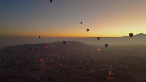 Drone view of Rose Valley near Göreme with hundreds of balloons preparing for takeoff, heated by bur
