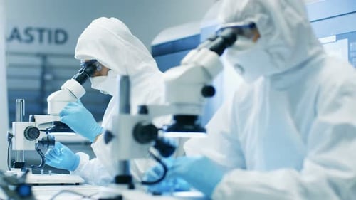Deux ingénieurs/scientifiques/techniciens vêtus de combinaisons stériles pour salles blanches utilisent des microscopes pour le composant Adj