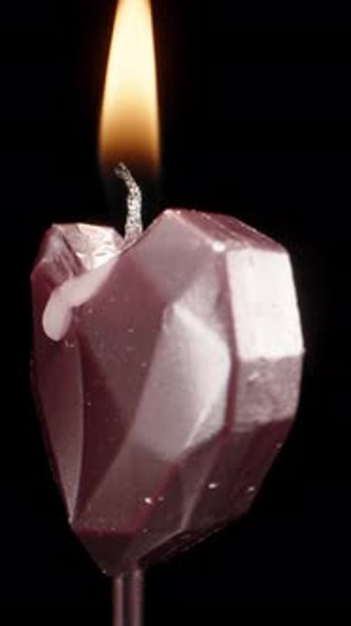 I set fire to a pink candle in the form of a heart on a black background, rotation. Vertical video.