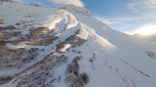 O drone FPV se aproxima de um flanco nevado de uma montanha ensolarada