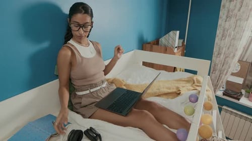Brunette College Girl Typing on Laptop and Putting on Headphones on Top Bunk