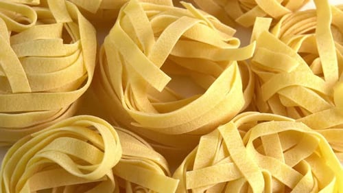 Uncooked italian pasta Tagliatelle or Fettuccine rotating background for advertising top view