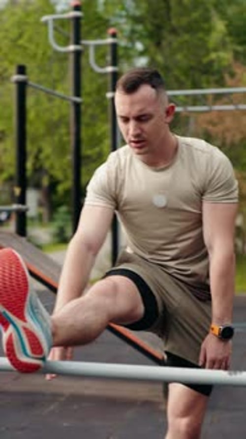 Man Stretching Leg on Bar in Outdoor Park