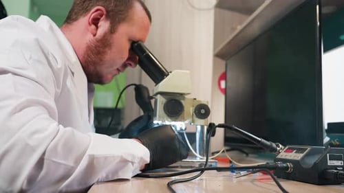 Technician Using Microscope to Inspect Circuit Board on Workbench