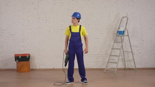 Full Length Video of a Smiling Young Worker Standing in the Room Under Renovation Raising the Drill