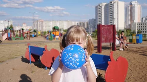 A Little Girl Inflates a Blue Balloon and Plays on the Playground