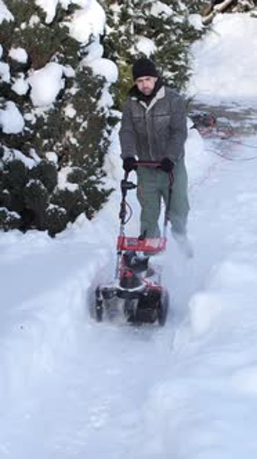 Vertical Video Man Operates Electric Snowblower Clearing Deep White Snow From a Residential Path