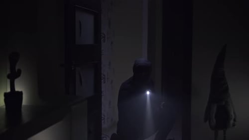 Shadowy Figure with Flashlight in Dimly Lit Interior