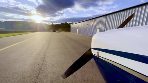 sunset push in beyond prop of piper cherokee 180 on tarmac outside hangar