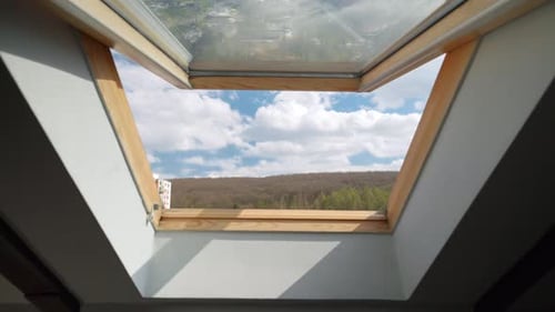 View from the open window at attic on blue sky with clouds.