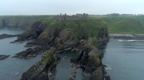 An aerial view of Dunnottar Castle on a misty and overcast day. Advancing towards the castle across